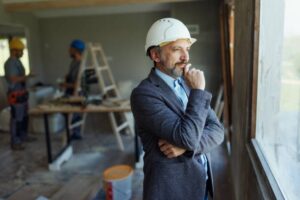 Construction business owner in a safety helmet reviewing project strategy while workers operate in the background